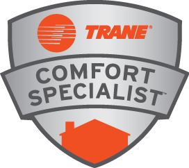 Shield-shaped badge with "Trane Comfort Specialist" in bold gray text. Features an orange Trane logo above and an orange house silhouette below, on a silver background.