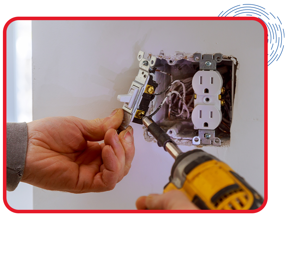 A person installs a light switch beside a power outlet in a wall. They use a yellow drill, demonstrating home electrical work in progress.
