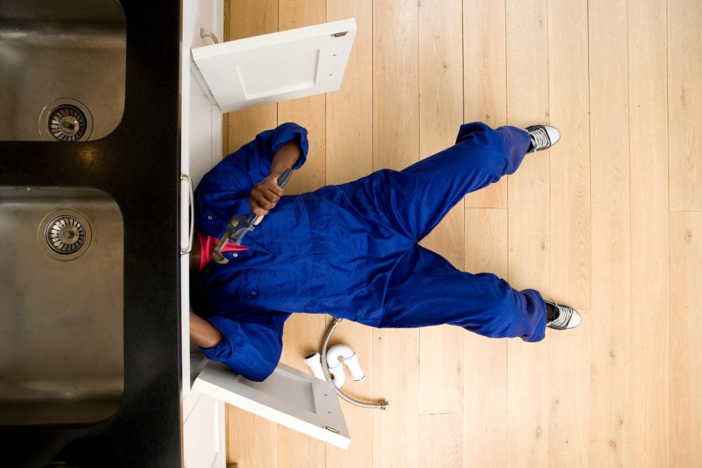 Plumber completing under-sink pipe repair as part of plumbing services.